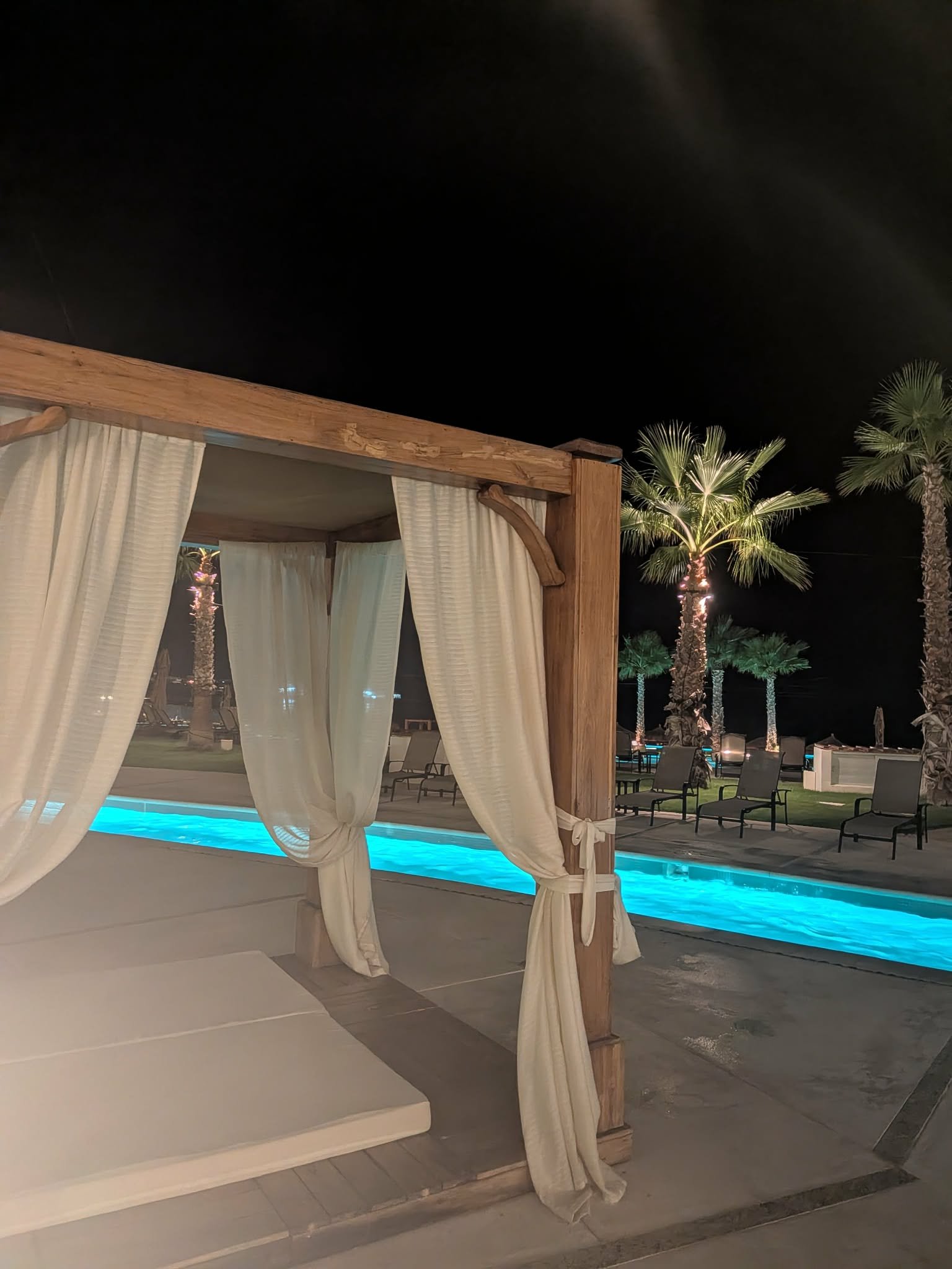 Curtained poolside cabana beside an illuminated pool at night
